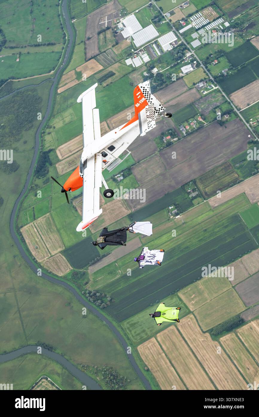 Un aeromobile Technoavia SM-92 Finist STOL vola sopra i terreni agricoli mentre i volanti con tuta alare scivolano in formazione a bordo in caduta libera. Foto Stock