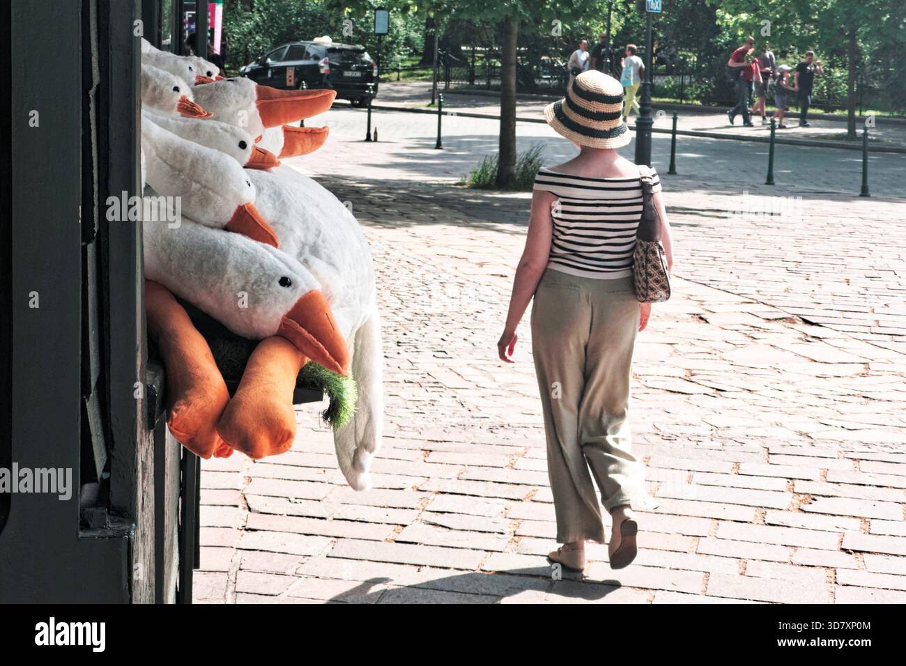 Donna che indossa un abito a righe che passa davanti a un chiosco con più peluche oche. Foto Stock