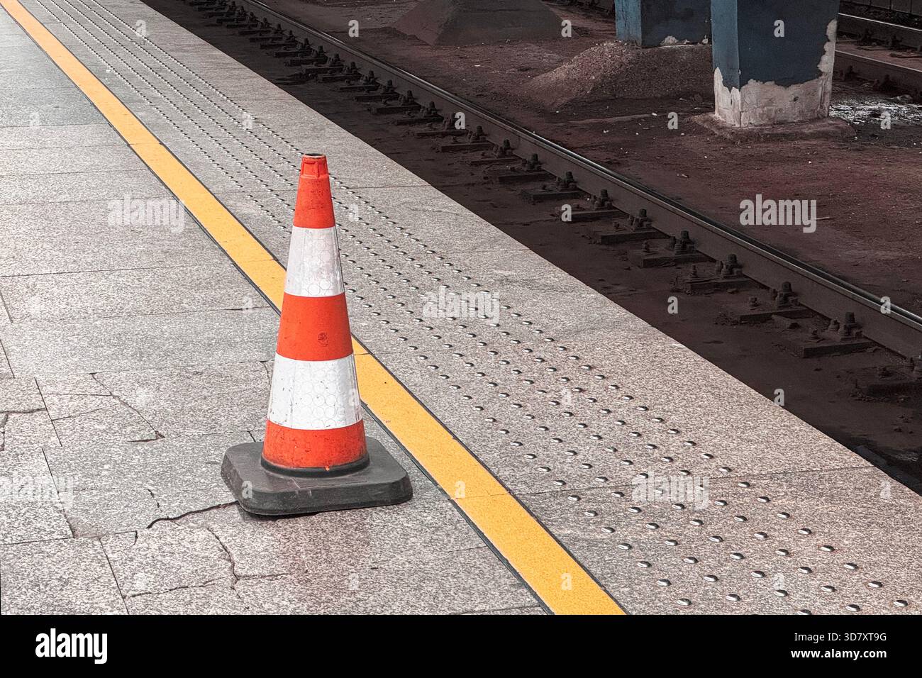 Il cono stradale arancione e bianco si trova su una piattaforma della metropolitana, accanto ai binari e a una linea di sicurezza gialla. Foto Stock