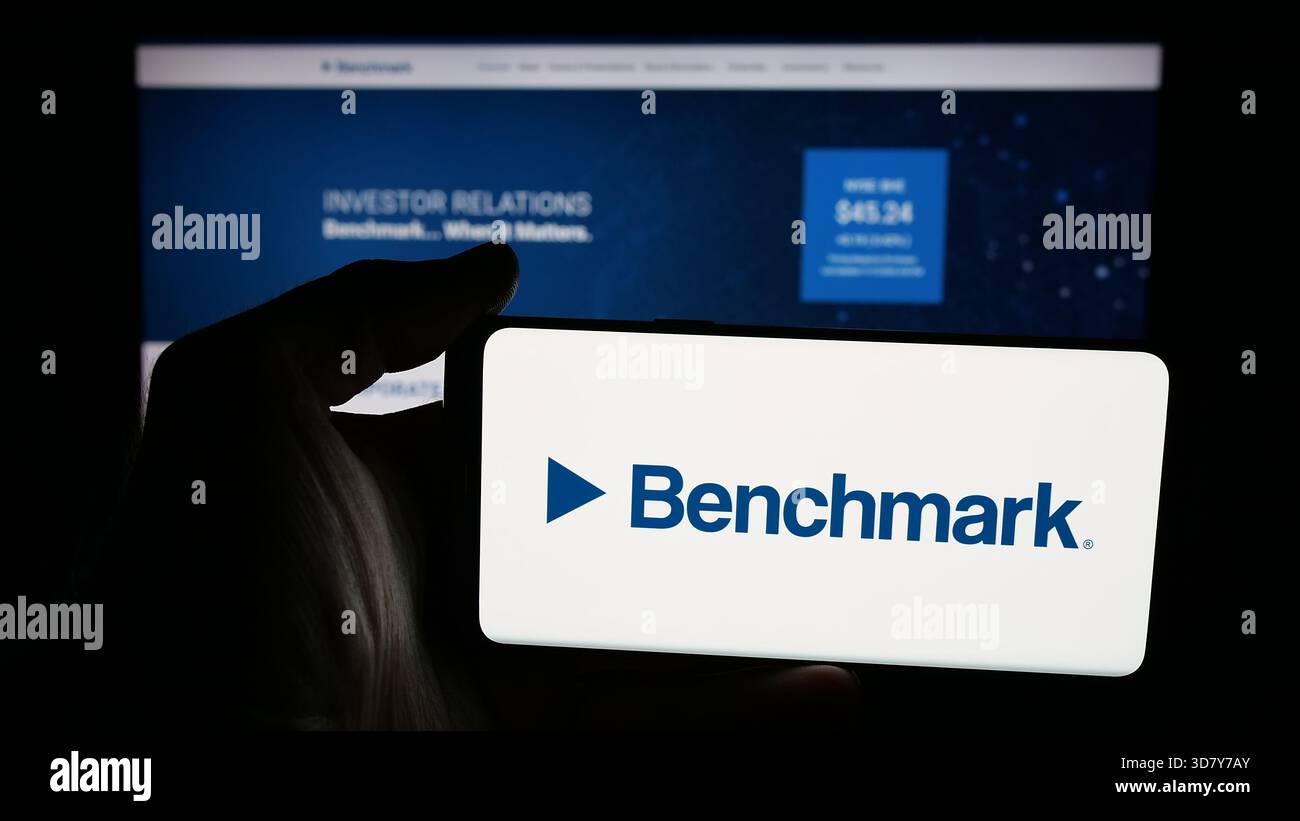 Stoccarda, Germania - 11-13-2025: Persona che detiene un telefono cellulare con il logo della società statunitense benchmark Electronics Inc. Sullo schermo davanti alla pagina Web. Foto Stock