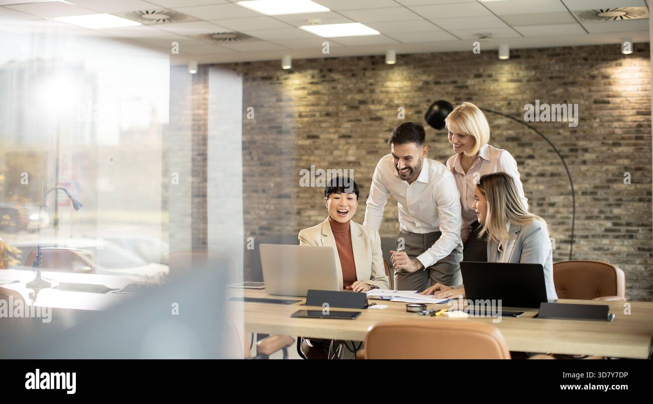 In un ufficio contemporaneo, quattro professionisti si impegnano in una discussione vivace intorno a un notebook. Le loro espressioni focalizzate mostrano il lavoro di squadra mentre condividono le idee Foto Stock