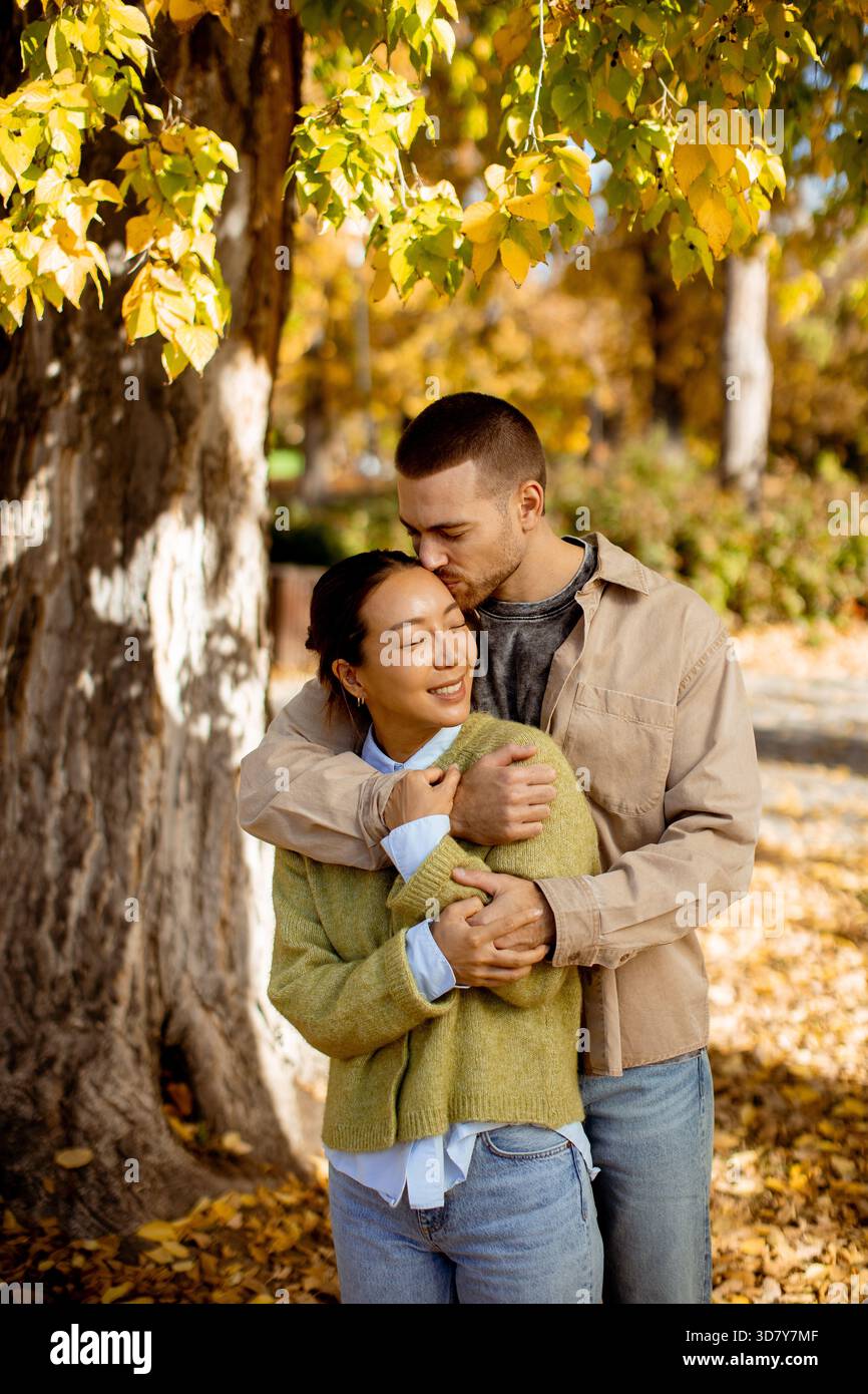 Una donna coreana e un uomo caucasico condividono un caldo abbraccio sotto i colorati alberi autunnali mentre si godono la serena atmosfera del parco. Foto Stock