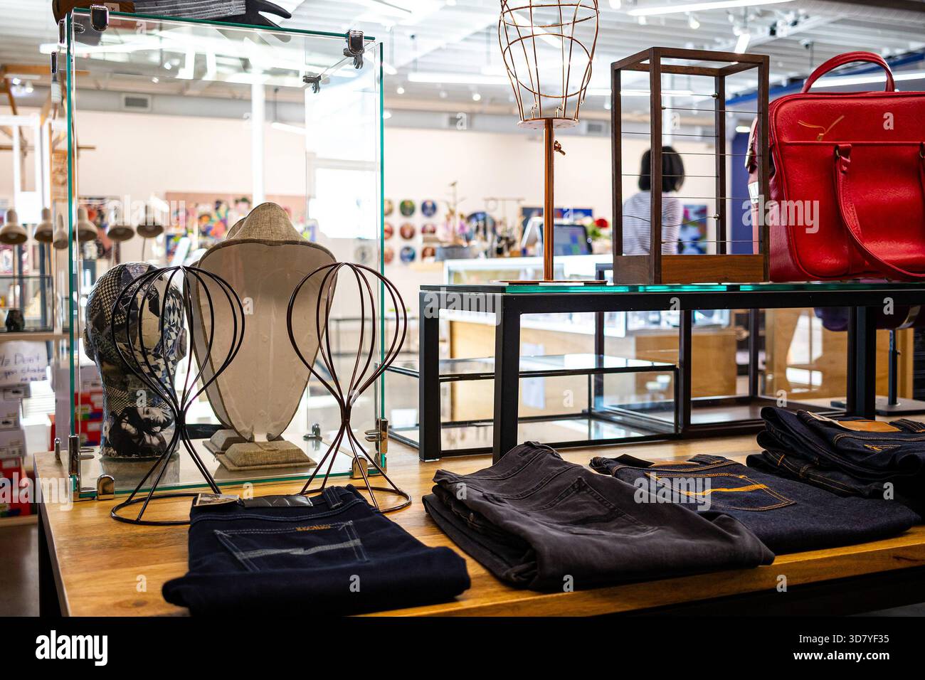 Interno di un negozio di articoli vintage o di beneficenza con articoli di seconda mano su uno scaffale o una panchina, tra cui jeans, borse e opere d'arte Foto Stock