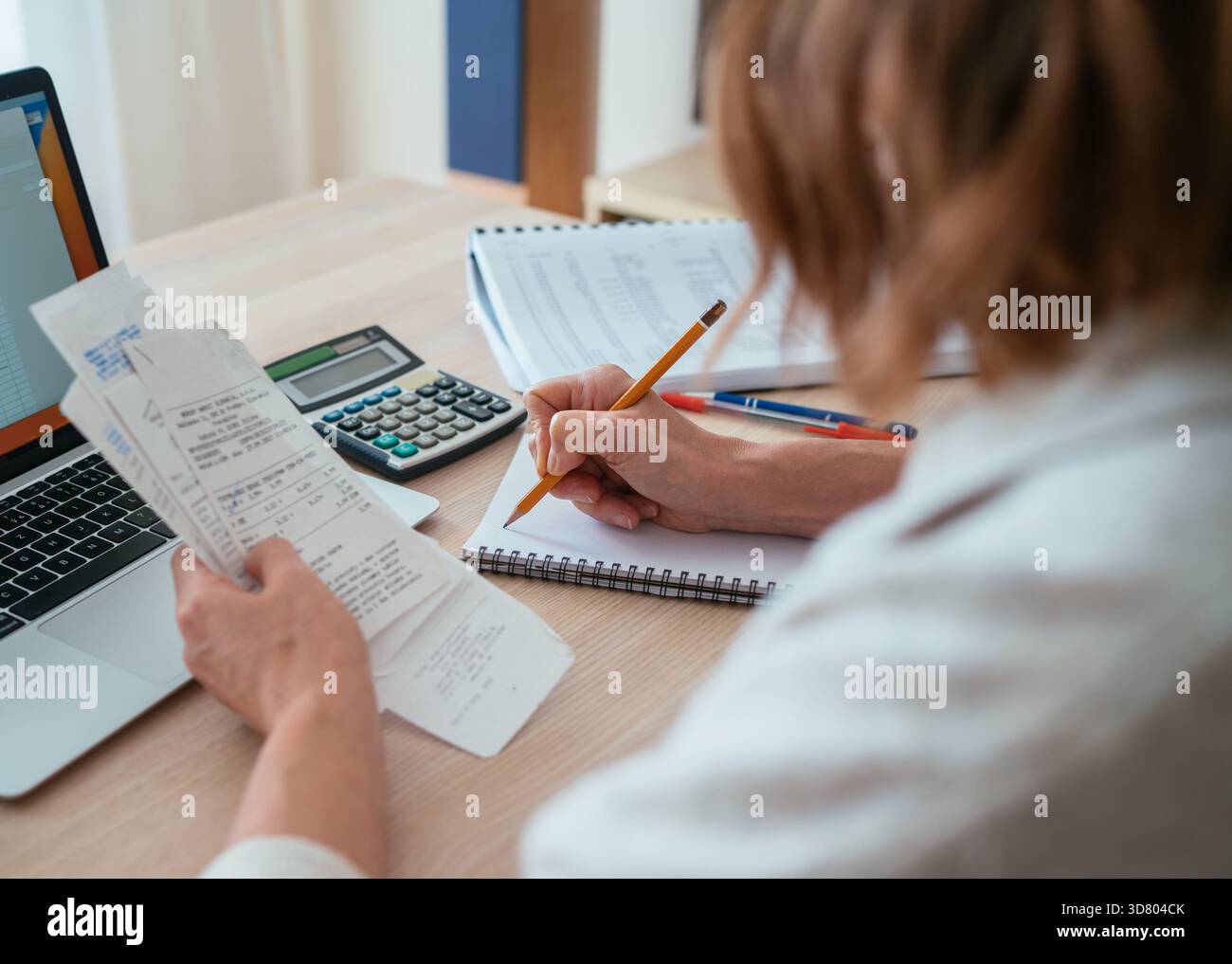 Donna che controlla le bollette mentre calcola le spese a casa. Vista a spalla della matita e della calcolatrice. Budget per la casa, gestione intelligente del denaro e pe Foto Stock