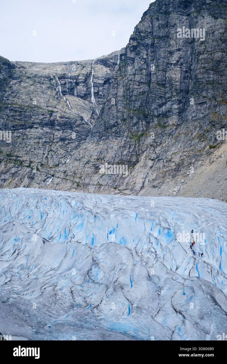 Ripida scogliera rocciosa con vibrante ghiaccio blu al ghiacciaio Nigardsbreen in Norvegia, suggestivo paesaggio glaciale nella natura artica. Foto Stock