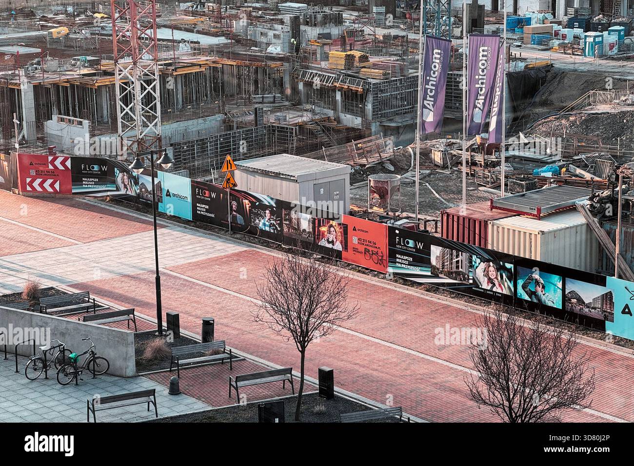 Vista aerea del cantiere urbano in corso con macchinari pesanti, ponteggi e striscioni promozionali lungo un passaggio pedonale. Foto Stock