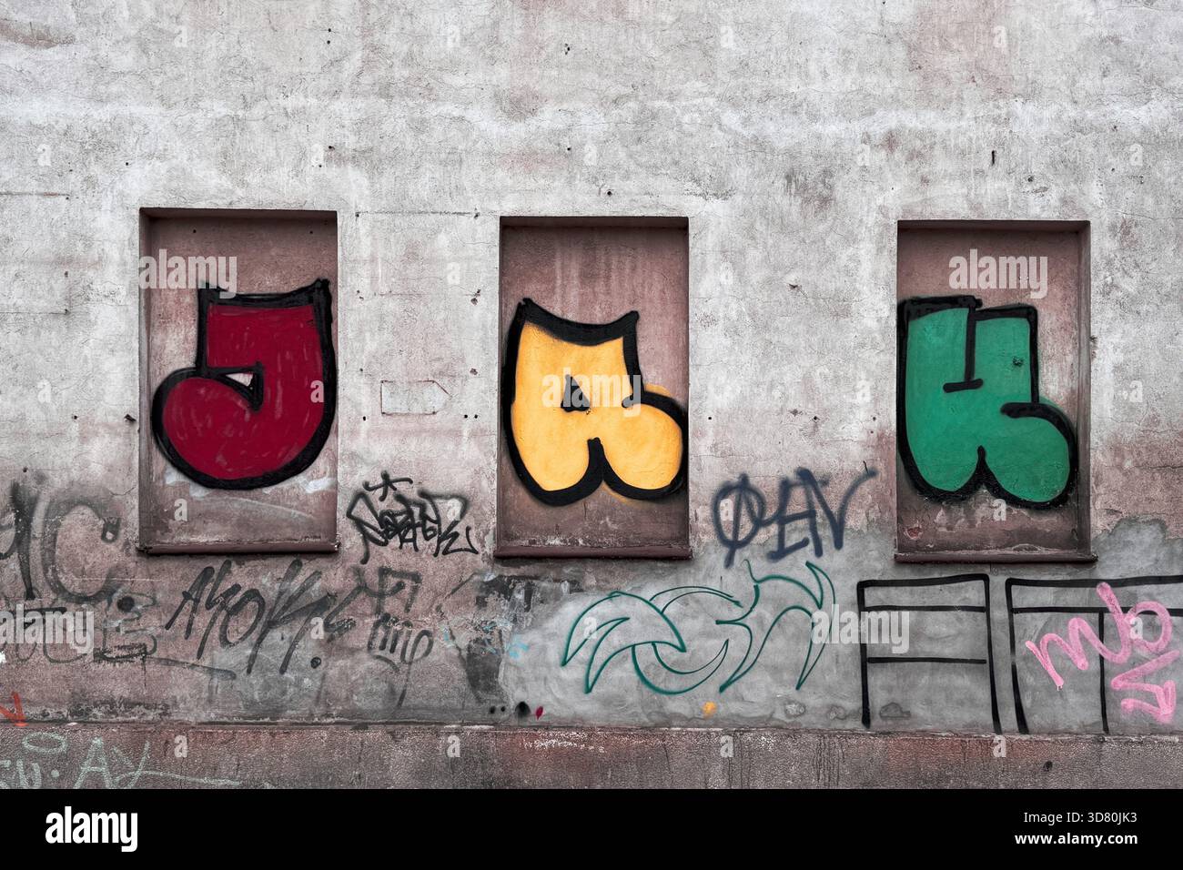 Lettere di graffiti colorate dipinte in vecchie incavi delle finestre su una parete in cemento indurito con etichette aggiuntive sotto. Foto Stock