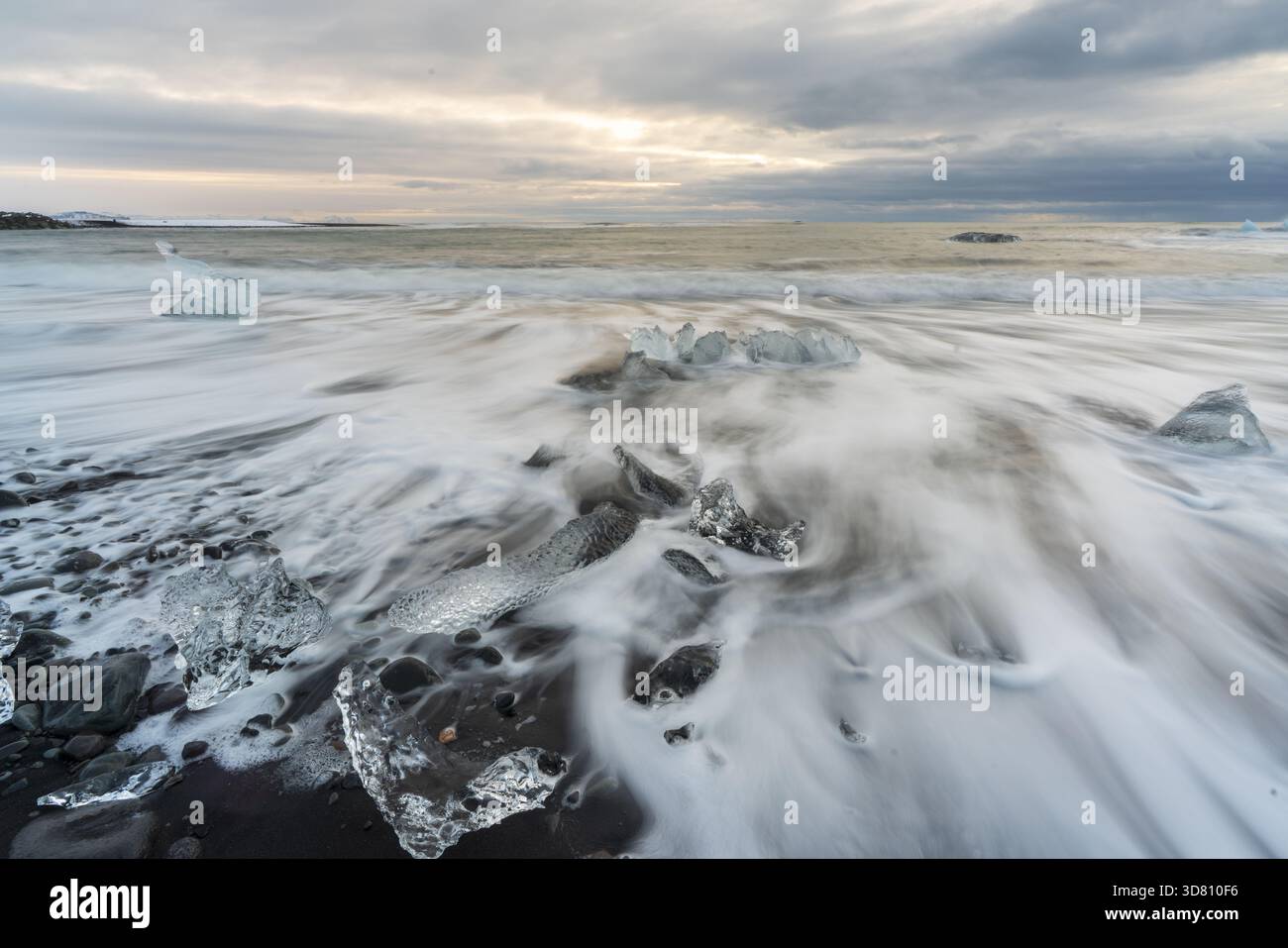 Vista dei frammenti di ghiaccio glaciale sparsi sulla sabbia vulcanica nera, mentre la marea scorre sotto un cielo spettacolare, Diamond Beach, Sveitarfelagid Foto Stock