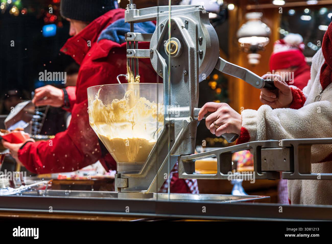 Vista ravvicinata di un fornitore che utilizza una macchina per imbuti di impasto in uno stand di cibo al mercatino di natale. Il batter è in fase di preparazione e porzionamento nella cucina festosa Foto Stock