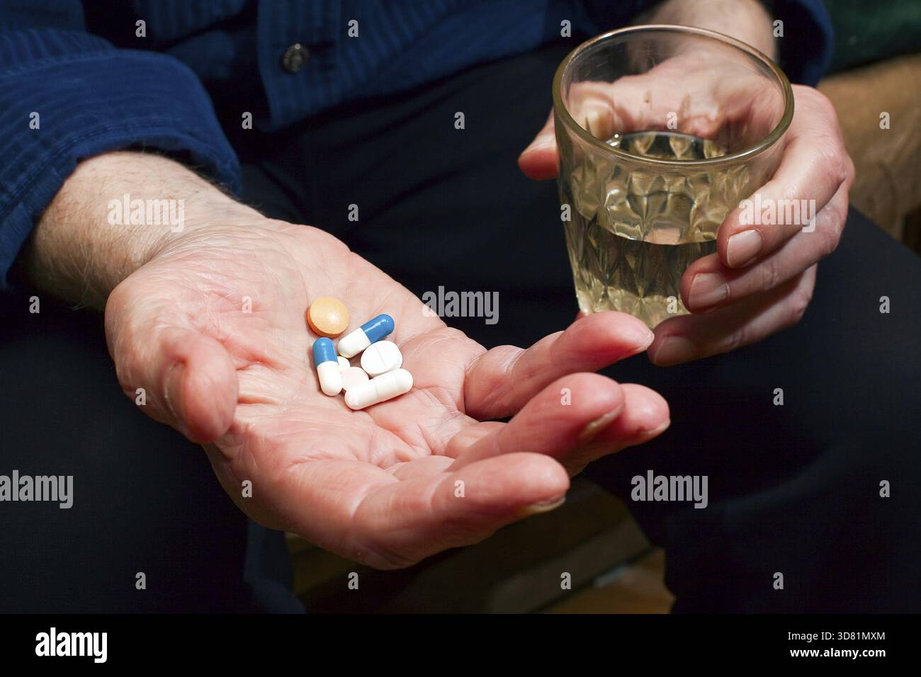 Primo piano con le mani di un vecchio con le pillole e un bicchiere d'acqua, sta per prendere delle medicine Foto Stock