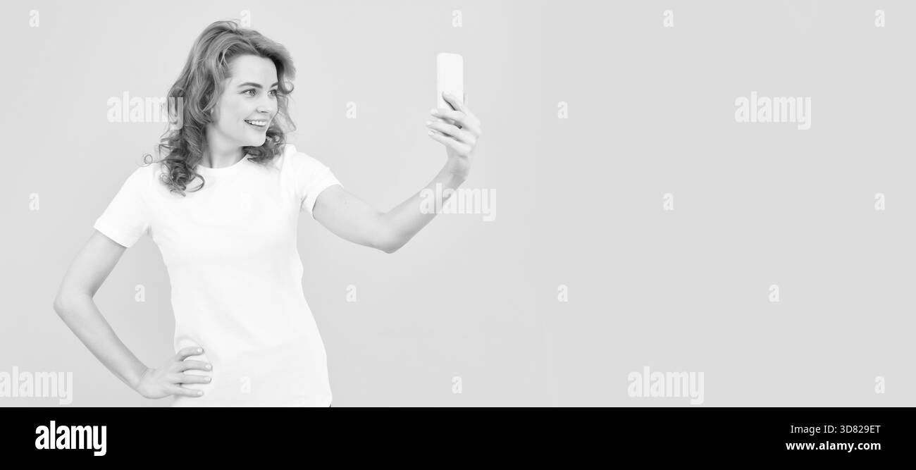 Felice ragazza sorriso a cellulare fotocamera sfondo giallo, selfie video. Donna isolato volto ritratto, banner con mock up spazio copia. Foto Stock