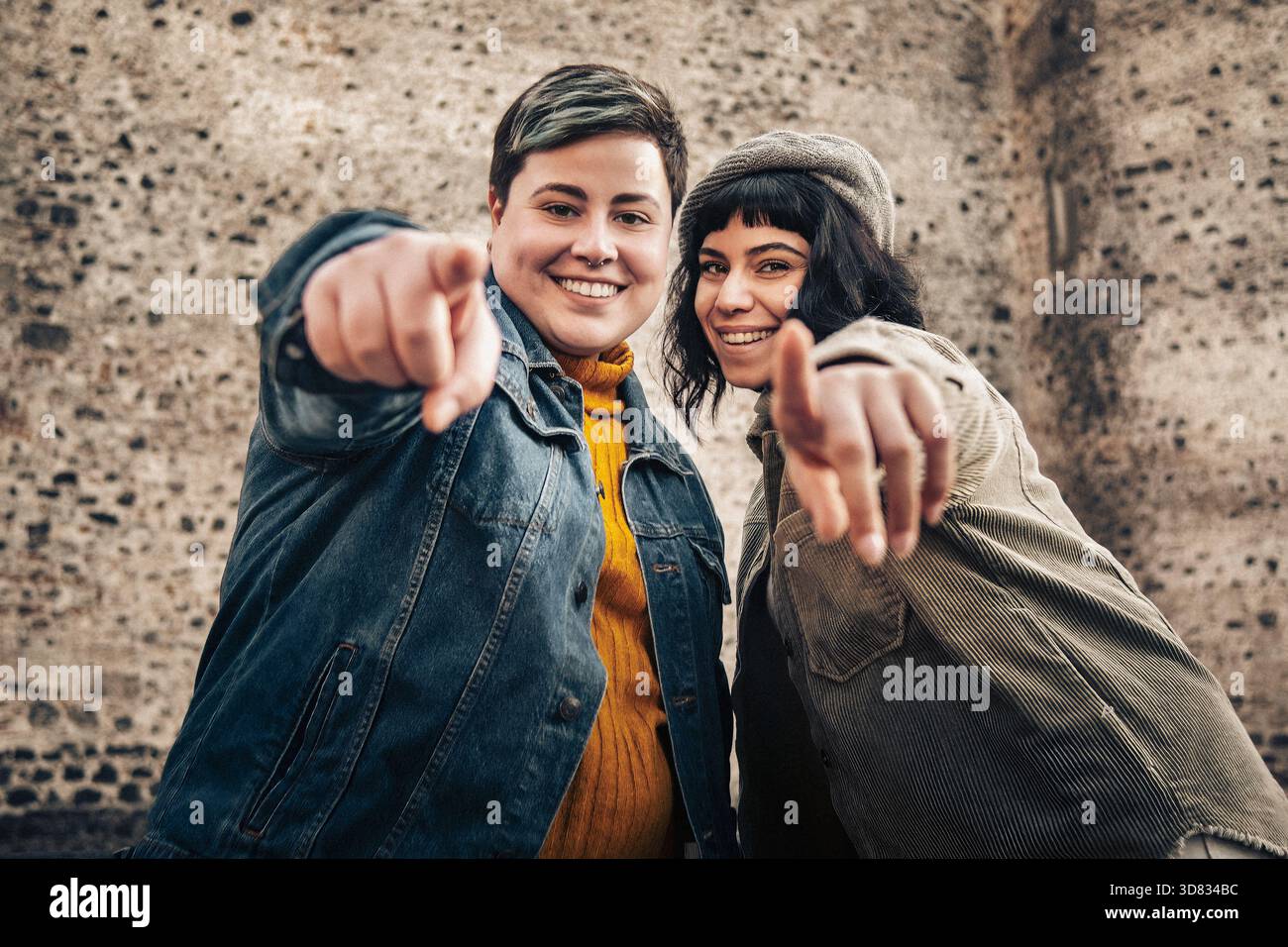 Due giovani donne che puntano verso la fotocamera con espressioni allegre, condividendo un momento di connessione e positività in un ambiente all'aperto. Foto Stock