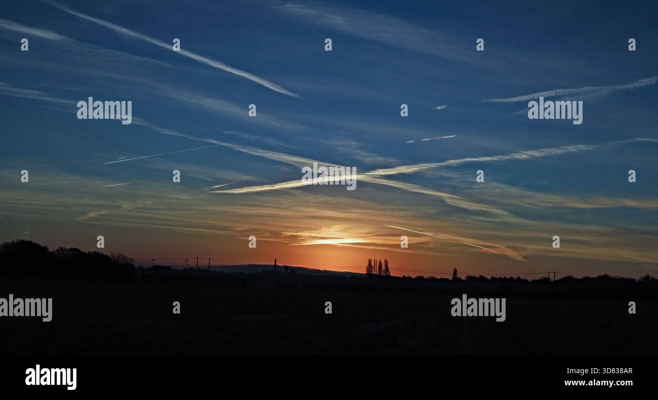 CW 9326 Croce nel cielo 26.11.2025. Mentre il sole sorge a est di Burscough nel Lancashire occidentale, illumina le piste dei vapori degli aerei sopra la t Foto Stock