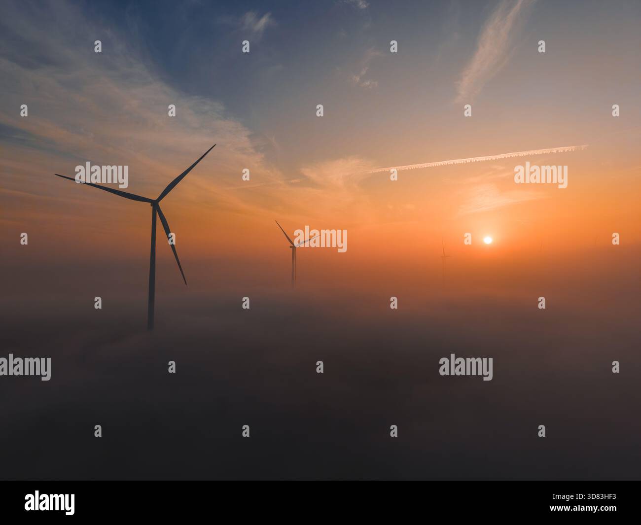 Turbine eoliche che si innalzano al di sopra di un paesaggio nebbioso all'alba con una luce calda Foto Stock