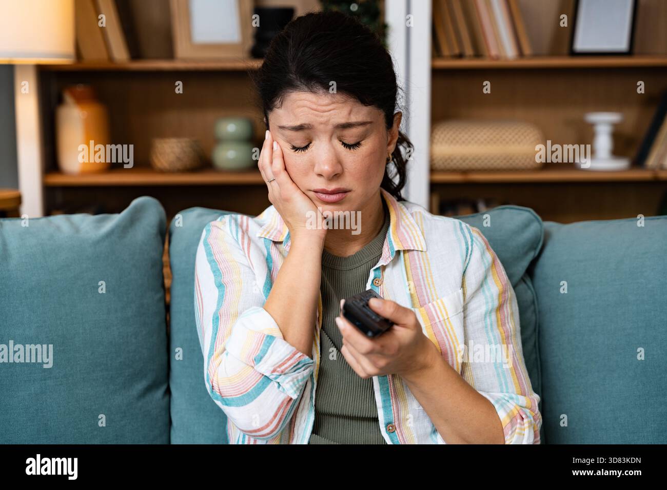 Donna preoccupata, seduta da sola a guardare notizie emotive in televisione, mentre tiene il telecomando, elaborando saldamente sentimenti difficili alla ricerca di un Foto Stock