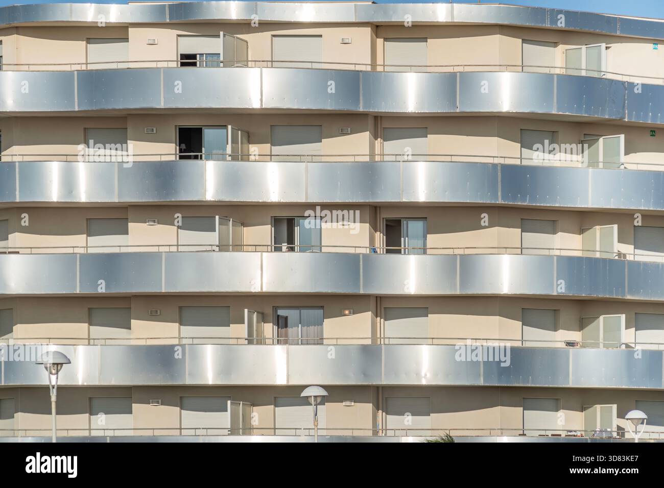 Primo piano della facciata di un moderno edificio di appartamenti curvo con finestre ripetitive, pareti beige e balconi in argento metallico Foto Stock
