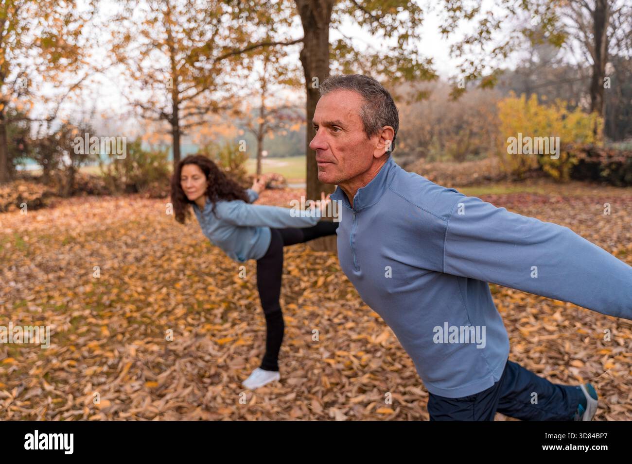 Uomo e donna senior si concentrano sull'equilibrio durante l'esercizio mattutino nel parco Foto Stock