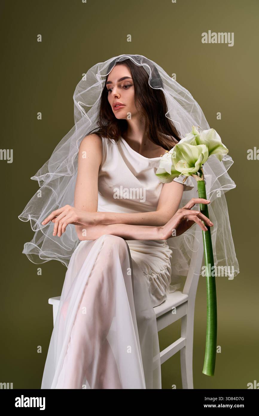 La giovane e bella sposa posa graziosamente con una suggestiva disposizione floreale, trasuda eleganza e gioia. Foto Stock