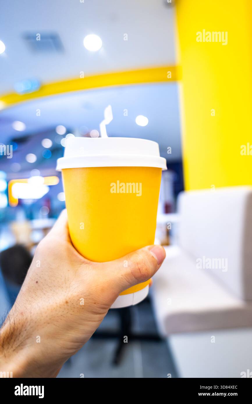 Tenere a mano una tazza di carta da asporto per un caffè o un tè e una bevanda calda nel caffè. Foto Stock