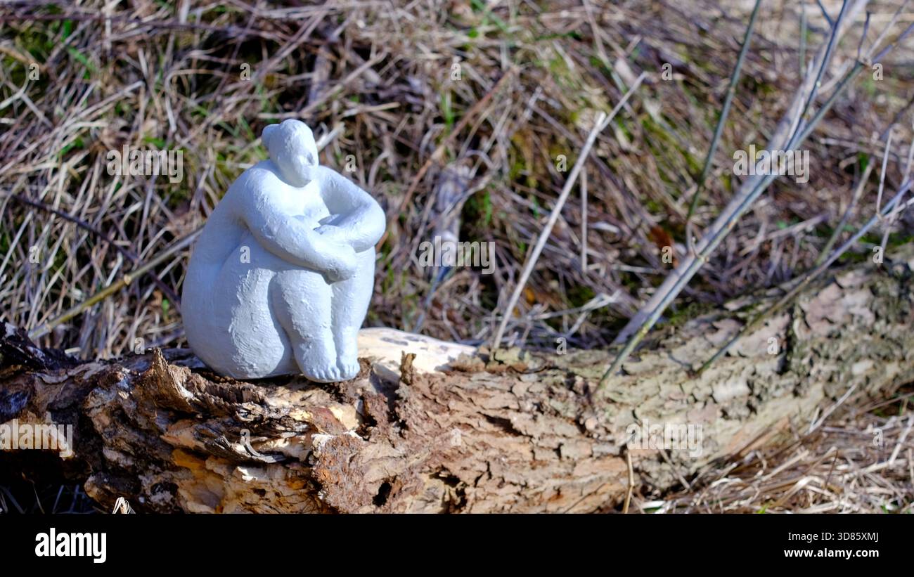 Statua bianca di gesso seduta su un tronco in natura. Foto Stock