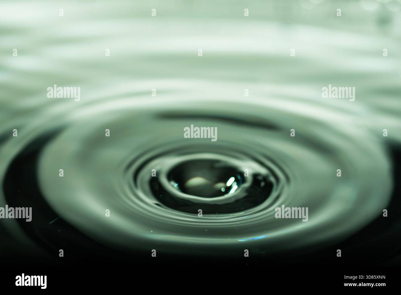 277.primo piano della superficie dell'acqua che mostra increspature concentriche dall'impatto centrale. Texture uniforme e qualità riflettente evidenziano il movimento fluido. T. Dominante Foto Stock