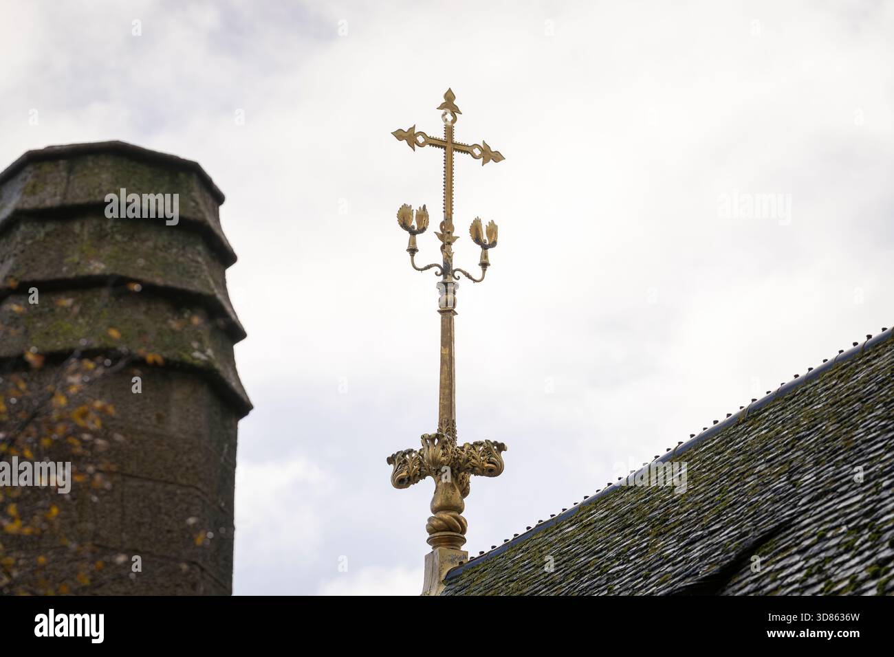 Tetto dorato decorato con croce gotica presso l'abbazia di Mont Saint-Michel. Croce decorativa gotica sul tetto e finitura scolpita contro un cielo nuvoloso. Foto Stock