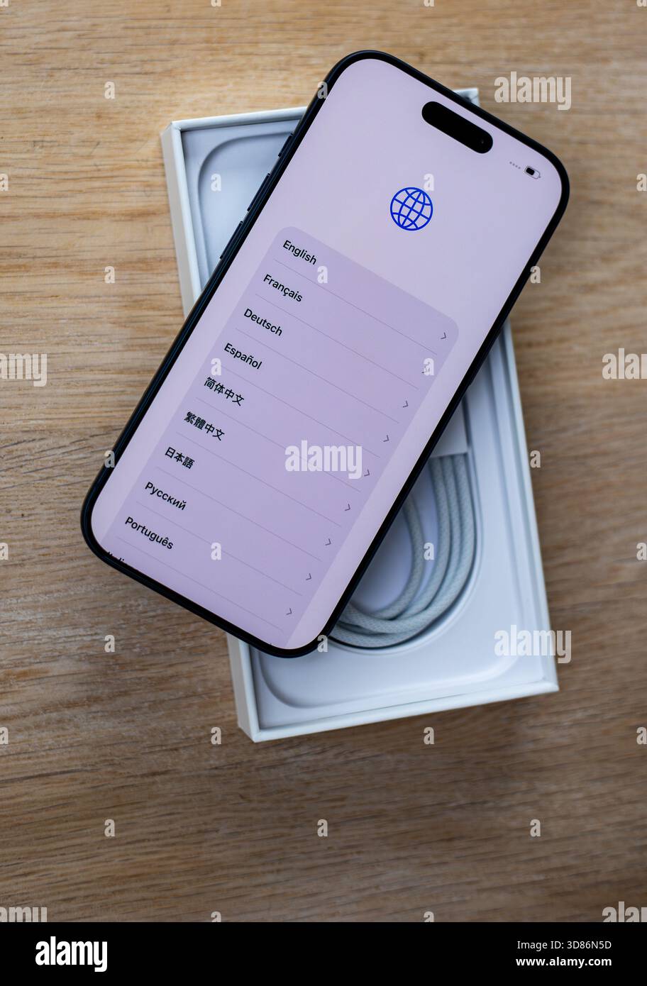 Smartphone che visualizza una schermata di selezione della lingua posizionata sulla parte superiore di una scatola aperta con accessori di ricarica su una superficie in legno Foto Stock