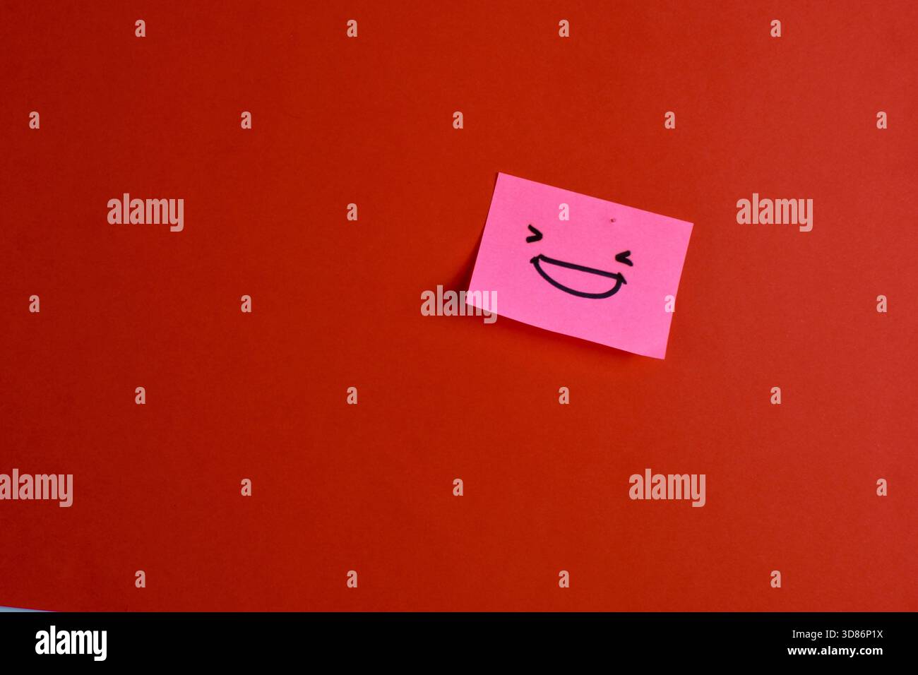 Nota adesiva rosa con faccia allegra su sfondo rosso, che enfatizza la gioia e l'espressione grazie al design minimalista e al forte contrasto cromatico. Foto Stock
