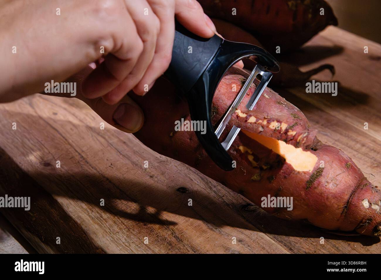 Rimuovere una striscia di pelle da una patata dolce Foto Stock