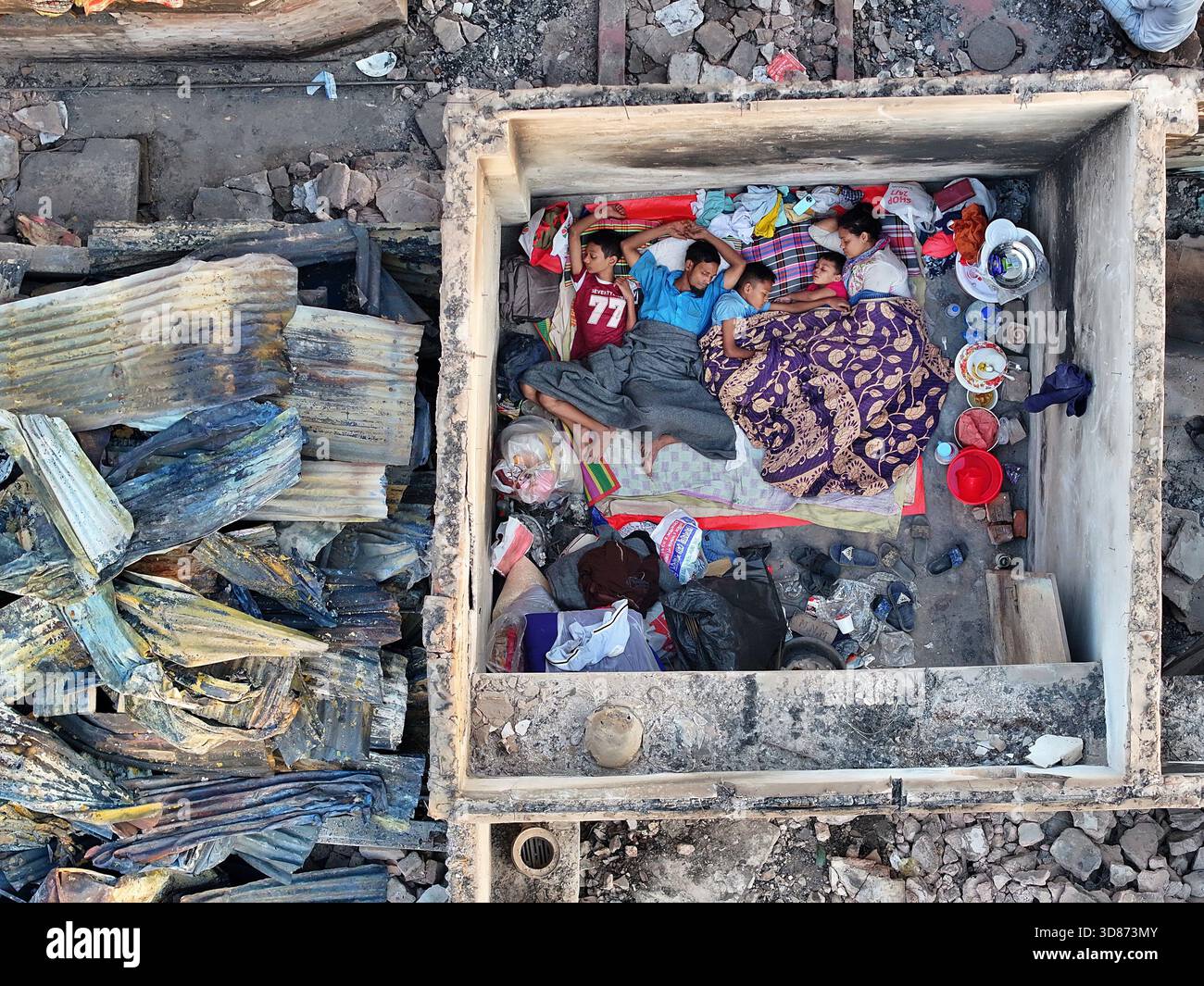 Dhaka, Bangladesh - 28 novembre 2025: Veduta aerea di una famiglia in cerca di rifugio in una struttura di cemento tra i resti carbonizzati del Korail Foto Stock