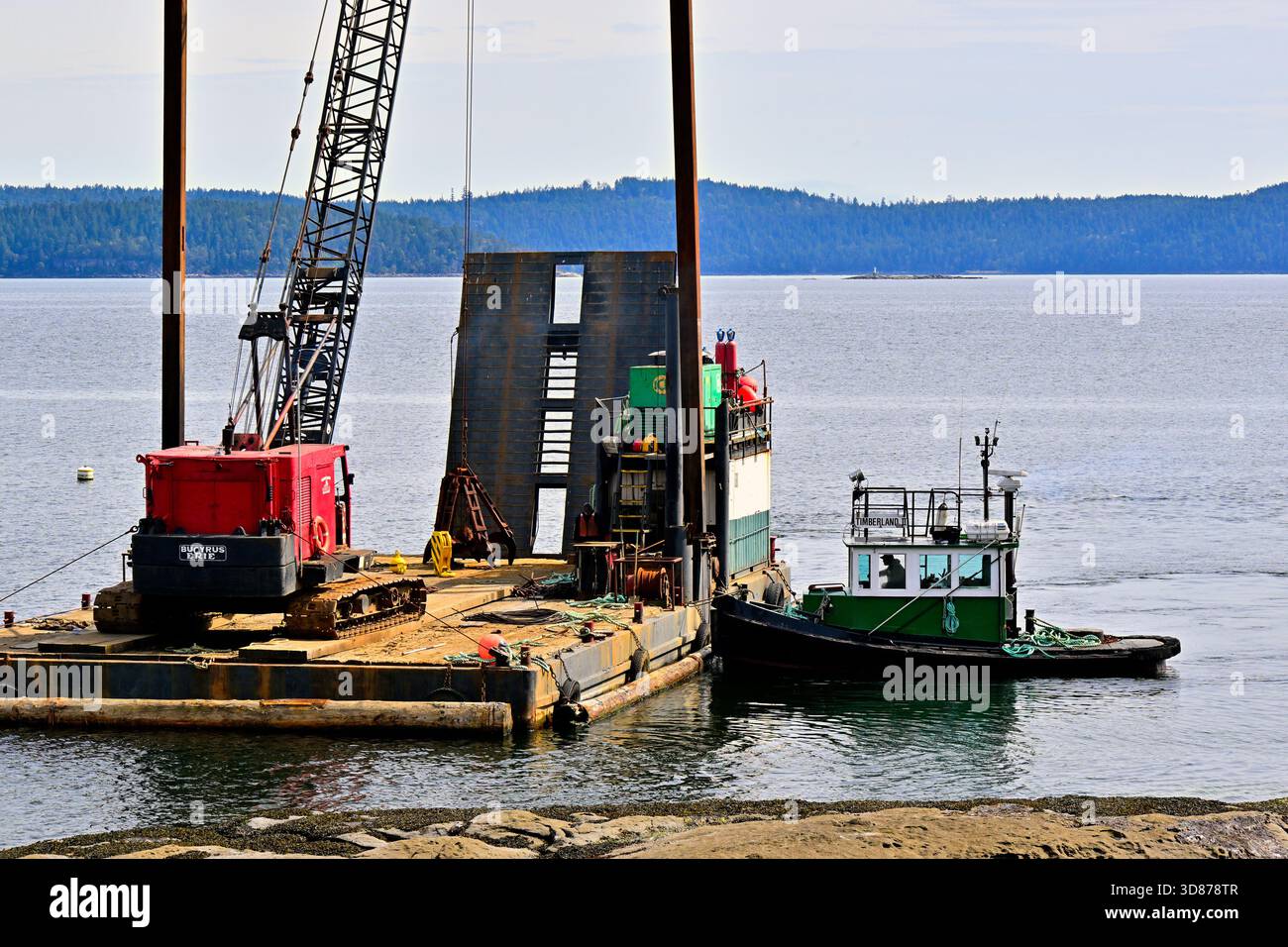 La costruzione costiera e le operazioni marine che comportano una chiatta e un rimorchiatore si svolgono su un tranquillo lungomare lungo le rive dell'isola di Vancouver, Foto Stock