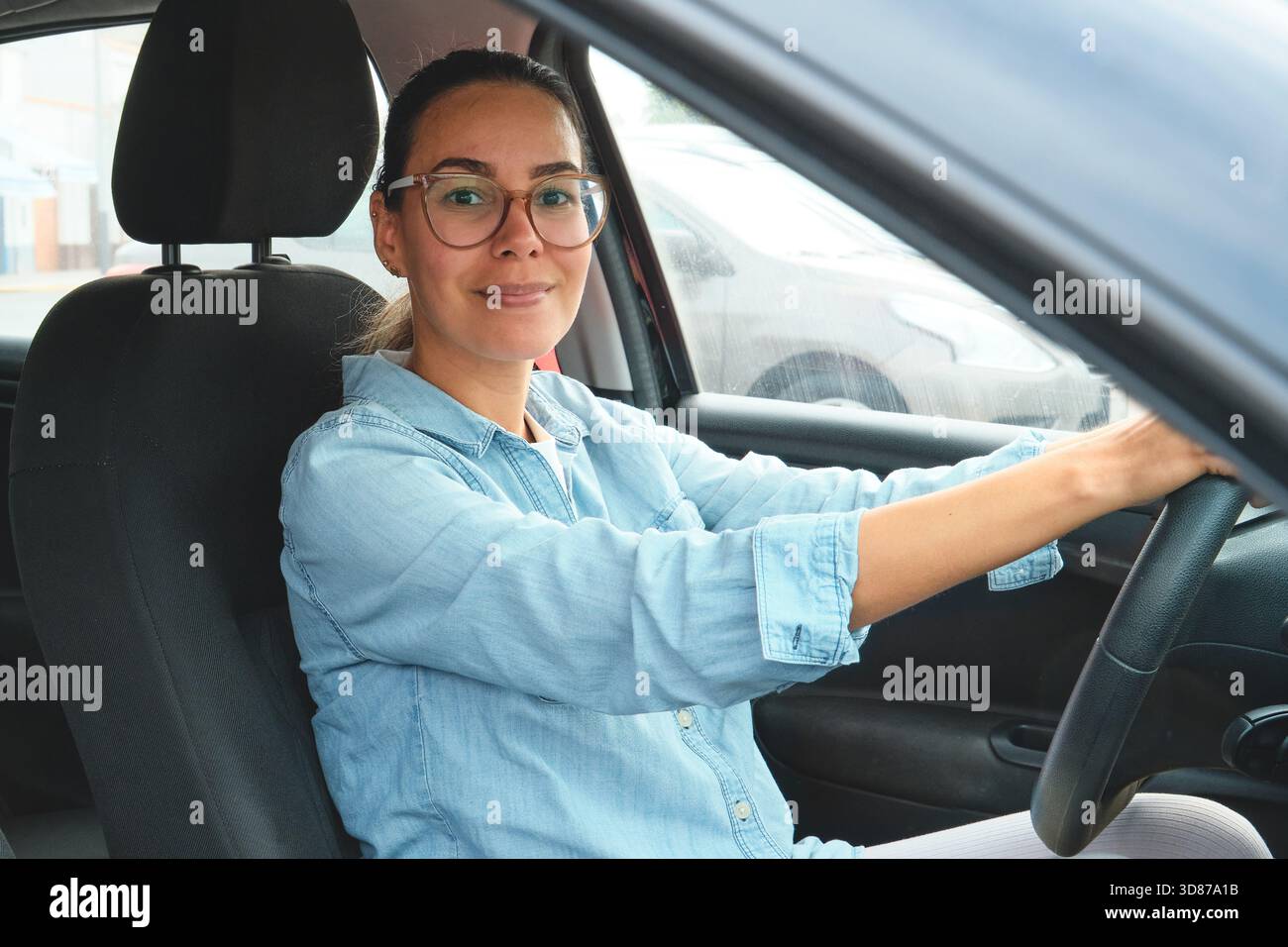 Donna che guida un'auto, guarda la fotocamera e sorride con un'espressione amichevole Foto Stock