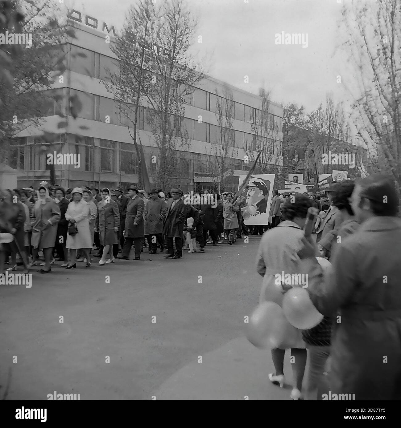 Slavyansk, Ucraina, URSS - 1970s: Una sfilata di manifestazioni festive in via Karl Marx (ora via Tsentralna). Le colonne dei residenti marciano oltre l'edificio modernista "Dom Byta" (House of Life Services). I partecipanti portano bandiere, palloncini, striscioni con slogan come "abbiamo bisogno di pace!" e ritratti di leader sovietici, tra cui Leonid Brezhnev. La gente è vestita con cappotti autunnali. Questa foto d'archivio in bianco e nero cattura i rituali ideologici, la moda e l'atmosfera sociale della tranquilla città industriale di Donbas. Foto Stock