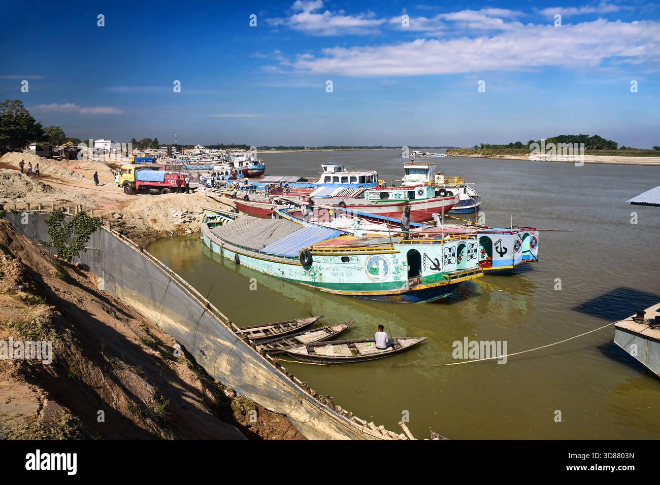 Porto colorato sul fiume con barche e attività sul molo presso un tranquillo canale navigabile durante la giornata di sole Foto Stock