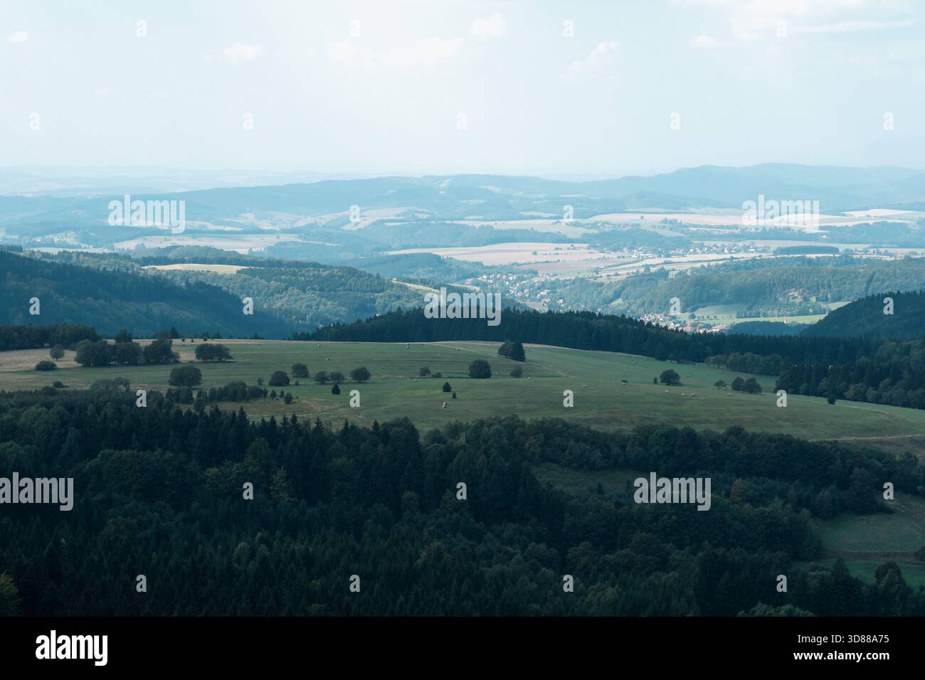 Ampio paesaggio di colline e vallate densamente boscose, con un piccolo borgo tradizionale visibile in lontananza Foto Stock