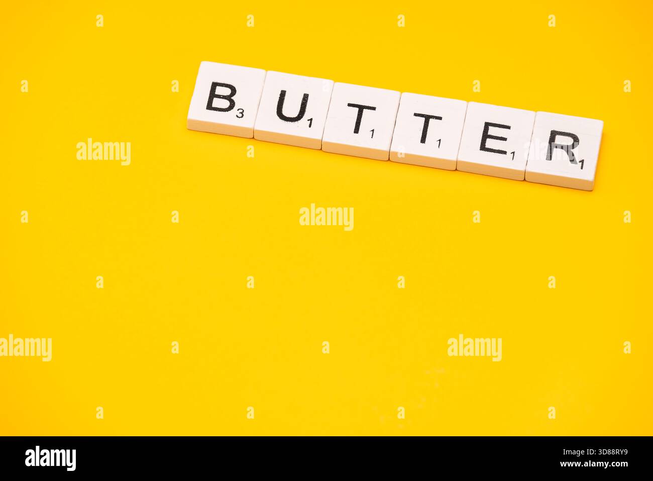 I wordtile scrivono la parola BURRO su uno sfondo giallo brillante. Foto Stock