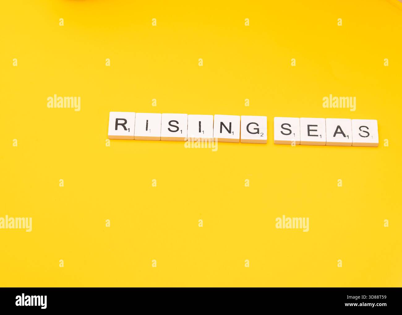 Le tessere della parola scrivono "MARI IN ASCESA” su sfondo giallo, simboleggiando la minaccia ambientale del cambiamento climatico. Foto Stock