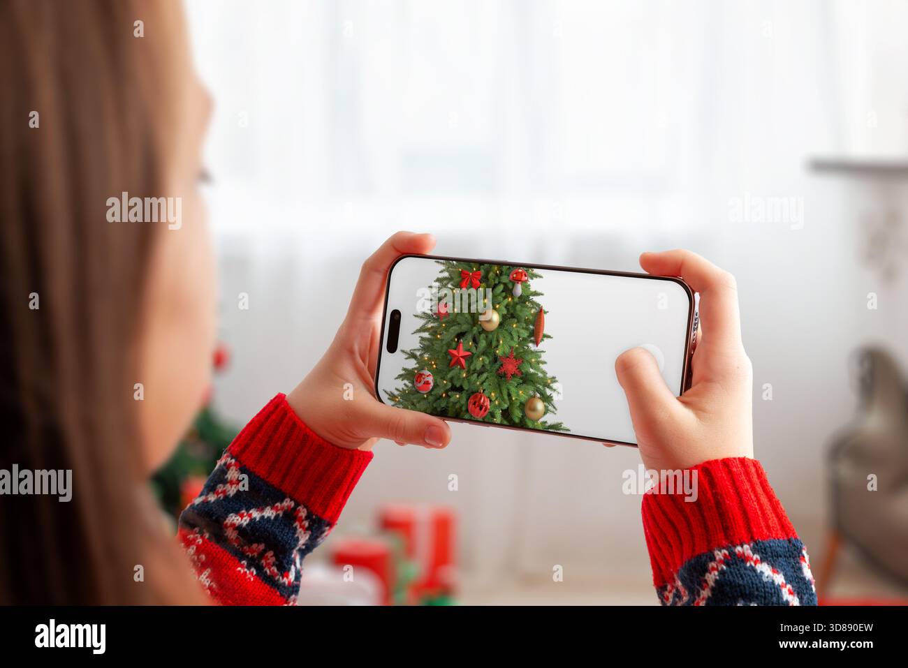 Donna che fotografa un albero di Natale decorato con lo smartphone, cattura gli ornamenti festivi e l'atmosfera accogliente delle vacanze in una luminosa dimora invernale Foto Stock