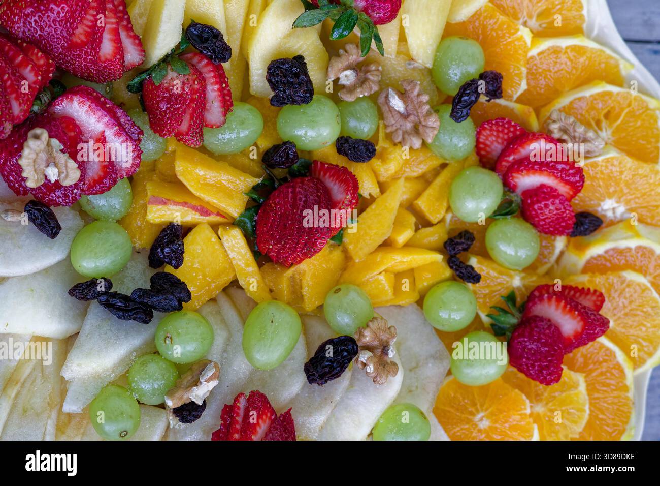 Frutta assortita a fette, tra cui fragole, arance, uva, mele, mango, uvetta e noci Foto Stock