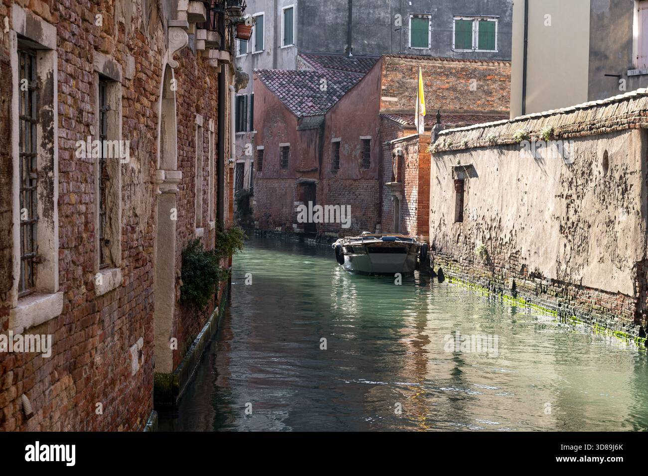 Stretto canale di Venezia, fiancheggiato da pareti in mattoni, fondazioni muschiate e piccole barche da lavoro, che creano un autentico atmosfera da laguna rustica. Foto Stock