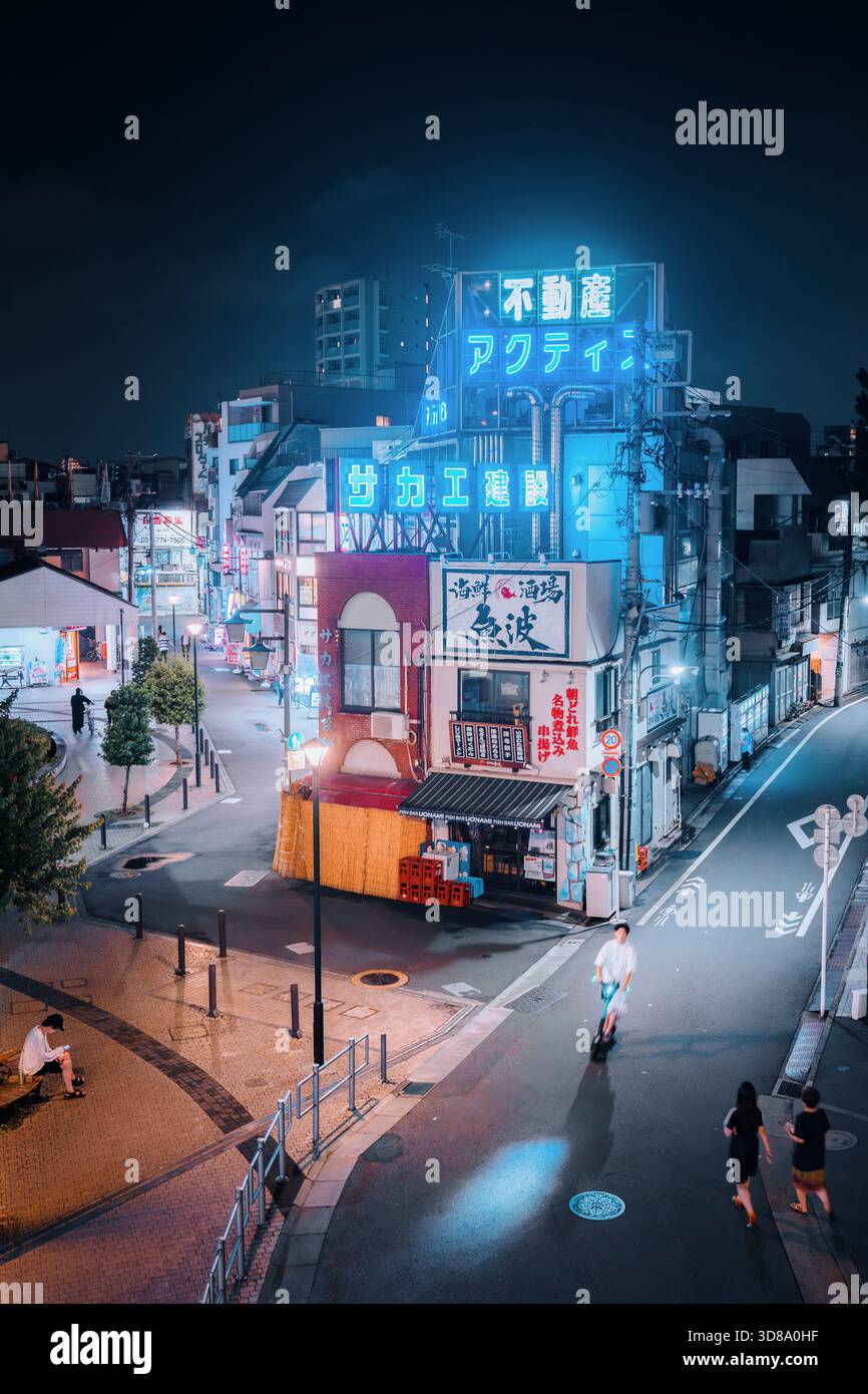 Le persone si godono una passeggiata serale e guidano monopattini elettrici su una strada illuminata da insegne al neon. Foto Stock