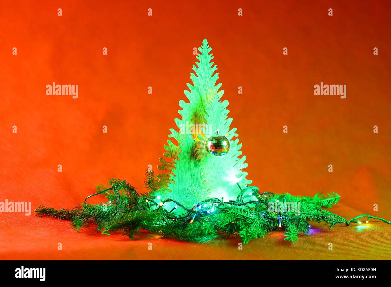 Un albero di Natale in legno si illumina di verde brillante, circondato da scintillanti luci delle fate e rami di pino. Foto Stock