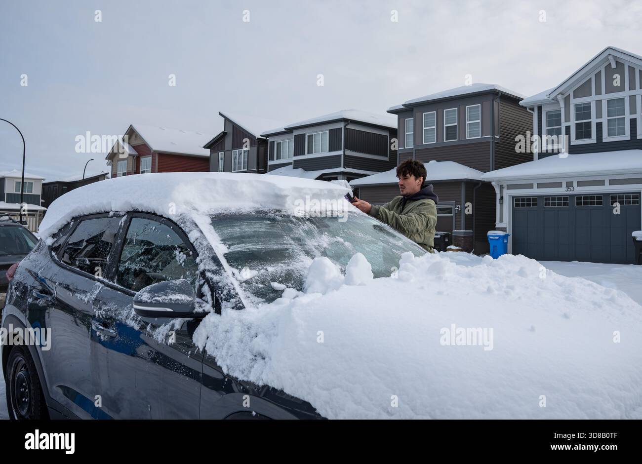 Un uomo raschia il ghiaccio e la neve dal parabrezza della sua auto dopo una tempesta di neve. Calgary, Alberta Foto Stock