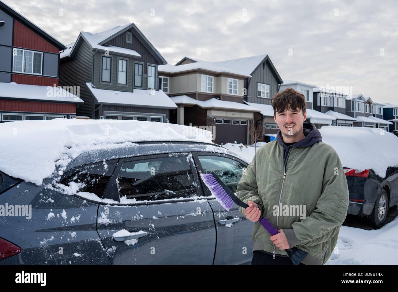 Uomo con spazzola che pulisce la neve pesante fuori dall'auto dopo una bufera nei sobborghi di Calgary, AB Foto Stock