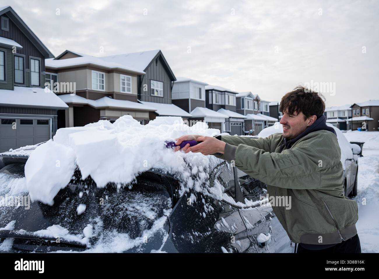 Uomo che pulisce la neve dalla macchina dopo una forte nevicata in un quartiere periferico. Calgary, Alberta Foto Stock