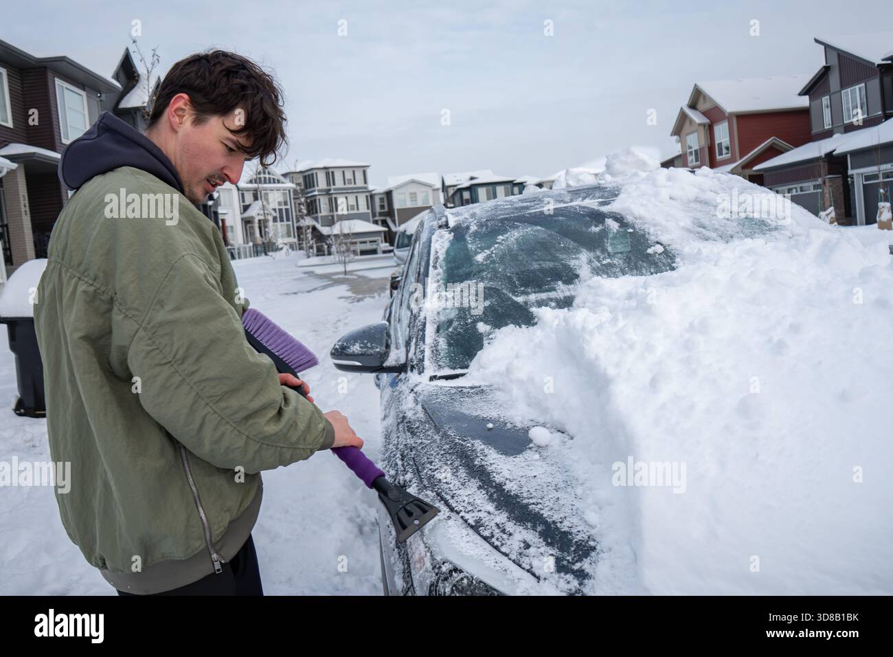 L'uomo sgombra la neve dalla macchina durante l'inverno nei dintorni con case intorno. Calgary, Alberta Foto Stock