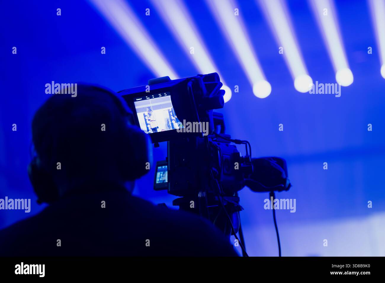 Una scena tecnica in live streaming con un operatore della videocamera che filma fasci illuminati sul palco mentre il video in tempo reale viene visualizzato sul monitor di bordo durante l'evento Foto Stock