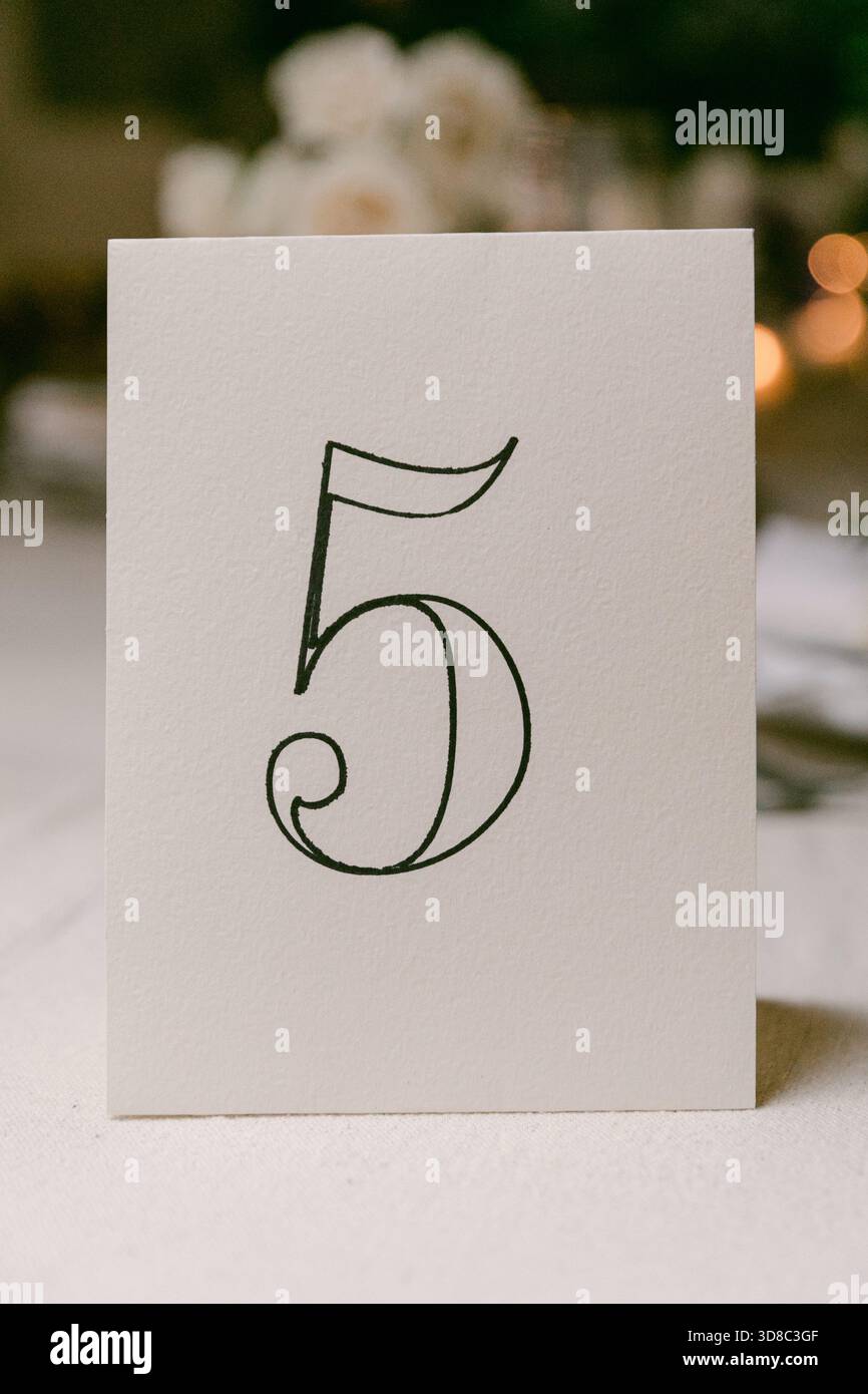 Il tavolo numero 5 e' elegantemente presentato su una superficie morbida, circondato da una luce calda durante un evento di festa serale. Foto Stock