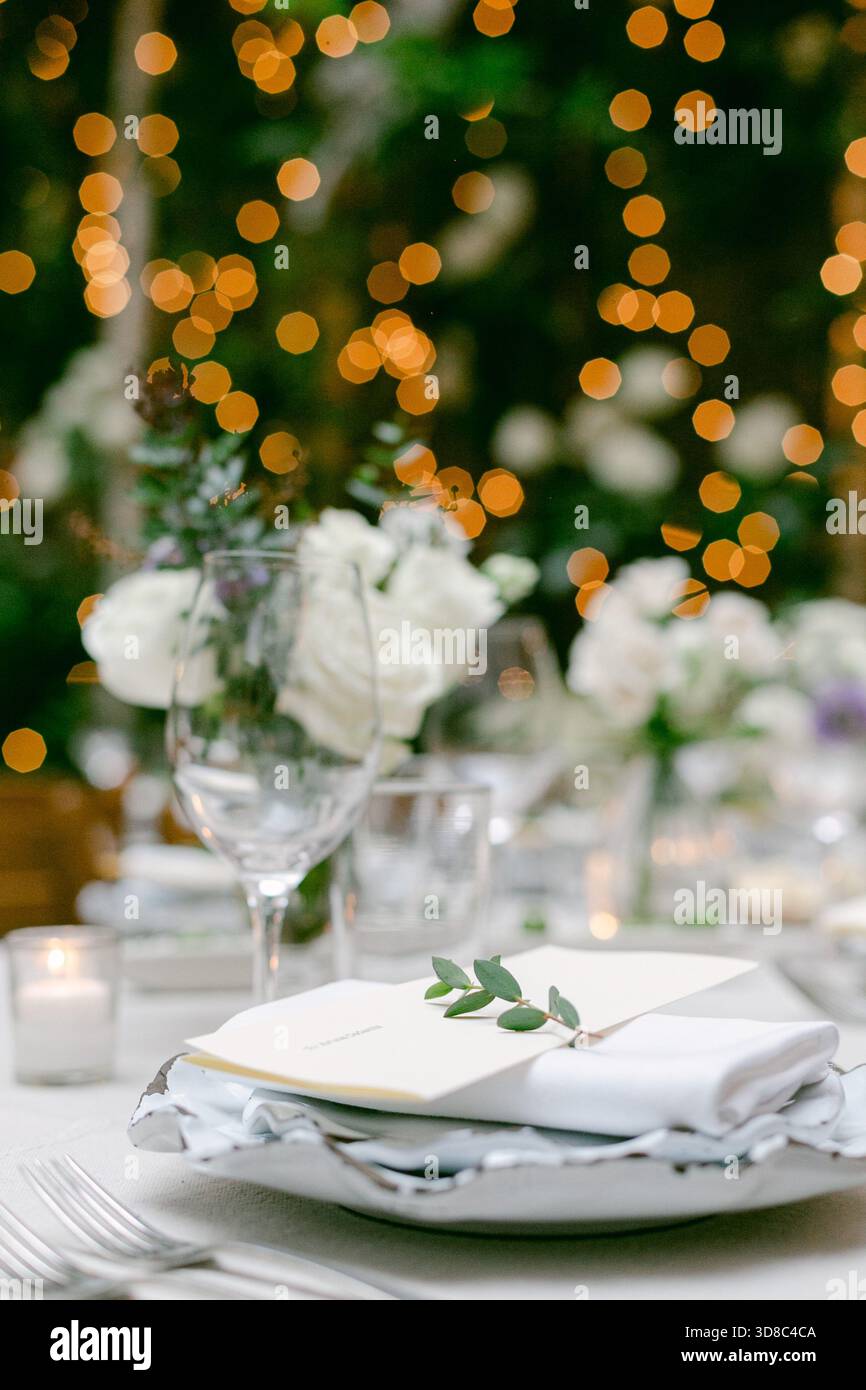 Un grazioso tavolo all'aperto mostra fiori bianchi, luci scintillanti e un elegante menu a carte. Foto Stock