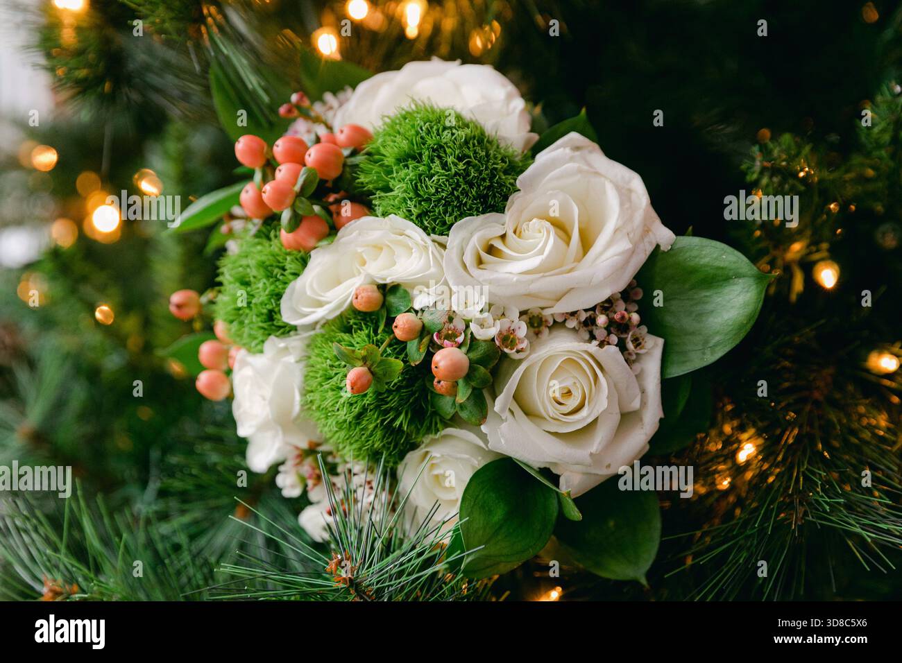 Bouquet delicato con rose bianche, accenti verdi e frutti di bosco, in mostra tra arredi festivi e luci calde. Foto Stock
